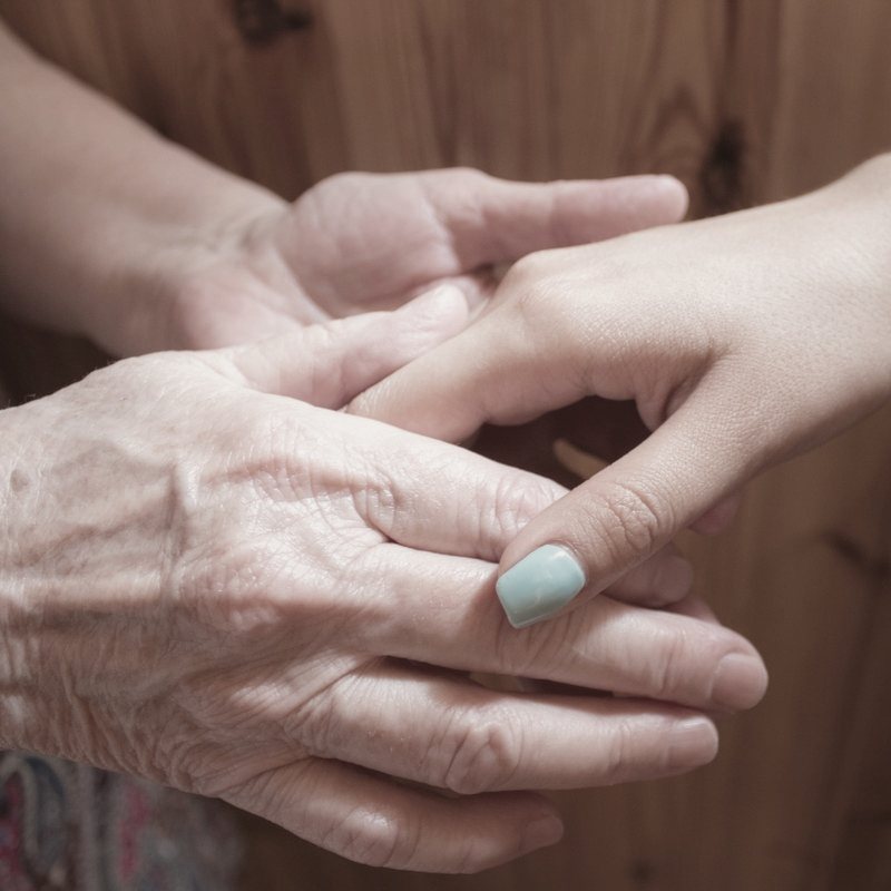 A younger hand gently holding an older woman's hand